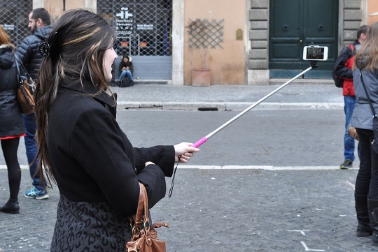 A woman uses a 'selfie stick' to take a selfie. (click for credit)